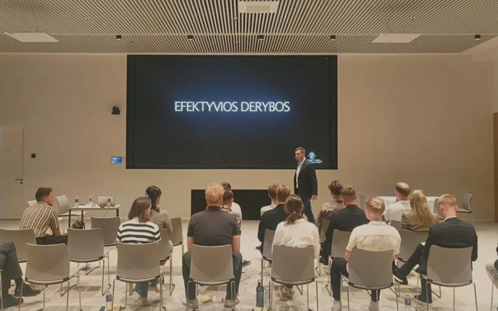 Derybų mokymų dalyviai klauso lektoriaus, ekrane užrašas „Efektyvios derybos“